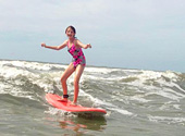 A young lady learns to surf with the help of Charleston Surf Lessons on Folly Beach.